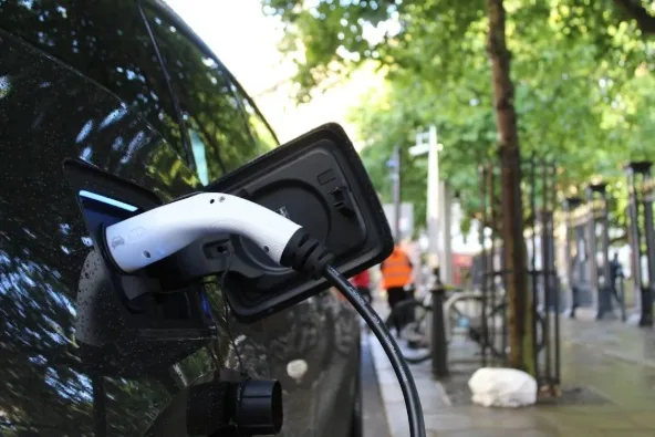 An electric car charging on a tree-lined street